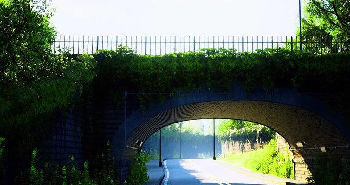 A peaceful morning scene features a winding road passing beneath a stone arch bridge. Lush greenery lines the path, creating a serene atmosphere in a rural setting.