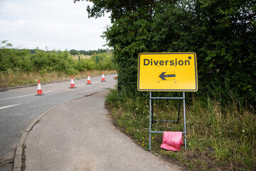 Yellow "Diversion" sign with a black arrow pointing left, positioned by the roadside. UK traffic sign indicating an alternative route due to roadworks or closures. Clear and visible.