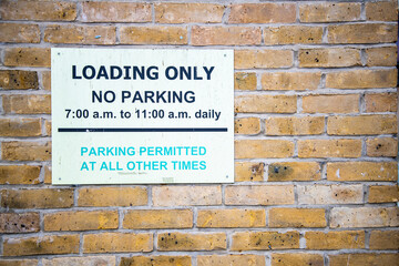 Loading only no parking sign on brick wall with time restrictions from 7 a.m. to 11 a.m. daily; parking permitted at all other times. Urban street sign in the UK.