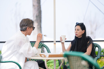 A Korean man and woman in their late 50s enjoy coffee and cake at a seaside cafe terrace with...