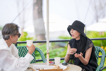 A Korean man and woman in their late 50s enjoy coffee and cake at a seaside cafe terrace with...
