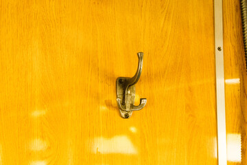 Close-up of a vintage metal coat hook on a polished wooden wall panel