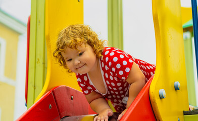 A young child wearing a red polka dot dress and yellow shoes plays happily on a playground slide The atmosphere is cheerful and colorful showcasing an enjoyable day outdoors