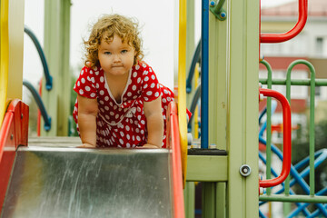 A young child wearing a red polka dot dress and yellow shoes plays happily on a playground slide The atmosphere is cheerful and colorful showcasing an enjoyable day outdoors