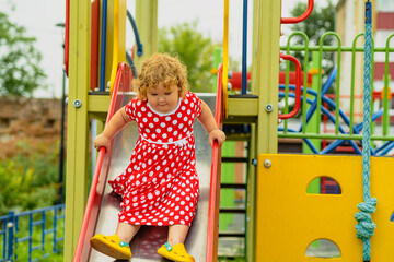 A young child wearing a red polka dot dress and yellow shoes plays happily on a playground slide The atmosphere is cheerful and colorful showcasing an enjoyable day outdoors