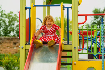 A young child wearing a red polka dot dress and yellow shoes plays happily on a playground slide The atmosphere is cheerful and colorful showcasing an enjoyable day outdoors