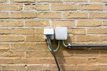 Outdoor electrical outlets mounted on a brick wall, connected by wires in protective conduits. The installation is intended for outdoor use and protected from weather conditions.