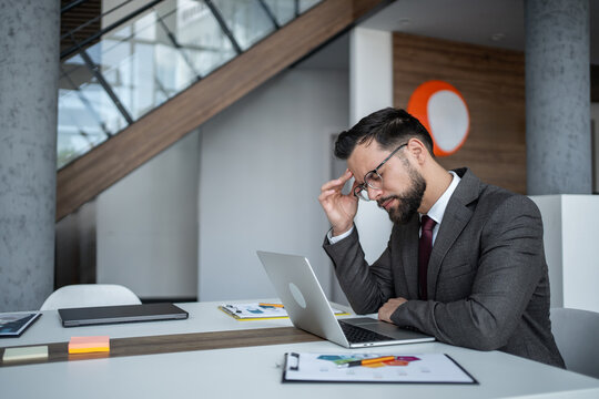 Stressed businessman having headache while working on laptop in office - Powered by Adobe