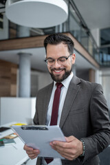 Smiling businessman reading documents on clipboard in office hallway