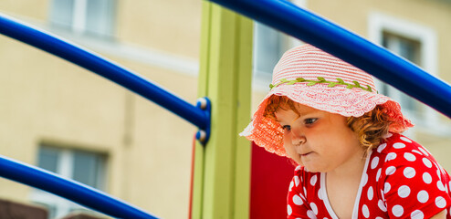 A young child wearing a red polka dot dress and a hat is climbing on colorful playground equipment The sun is shining in a vibrant outdoor park setting creating a joyful atmosphere