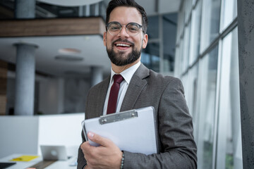 Smiling businessman holding clipboard in modern office building