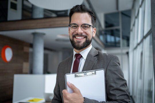 Portrait of smiling businessman holding clipboard in office hallway