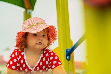 A young child wearing a red polka dot dress and a hat is climbing on colorful playground equipment The sun is shining in a vibrant outdoor park setting creating a joyful atmosphere