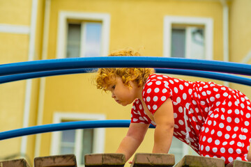 A young child wearing a red polka dot dress and a hat is climbing on colorful playground equipment The sun is shining in a vibrant outdoor park setting creating a joyful atmosphere