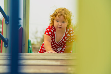 A young child wearing a red polka dot dress and a hat is climbing on colorful playground equipment The sun is shining in a vibrant outdoor park setting creating a joyful atmosphere