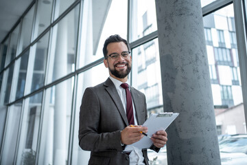 Smiling businessman holding clipboard in modern office building