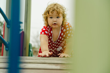 A young child wearing a red polka dot dress and a hat is climbing on colorful playground equipment The sun is shining in a vibrant outdoor park setting creating a joyful atmosphere
