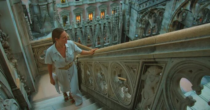 Visitor climbs white marble staircase surrounded by gothic elements at Milan Cathedral