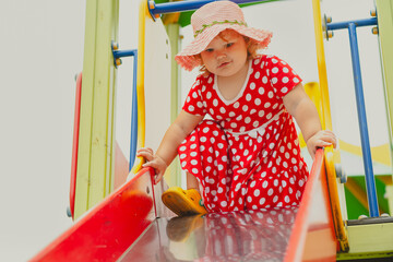 A happy kid in a red polka dot dress is sliding down a playground slide Bright colors surround her and the atmosphere is joyful during a sunny day with playful clouds
