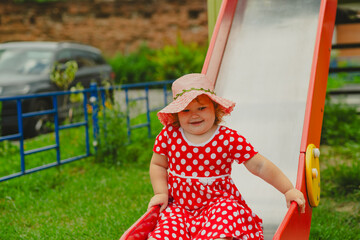 A happy kid in a red polka dot dress is sliding down a playground slide Bright colors surround her and the atmosphere is joyful during a sunny day with playful clouds