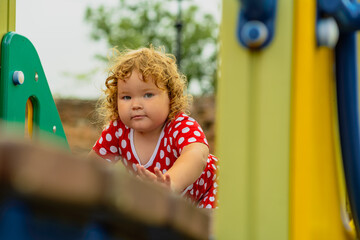 A young child wearing a red polka dot dress and a hat is climbing on colorful playground equipment The sun is shining in a vibrant outdoor park setting creating a joyful atmosphere