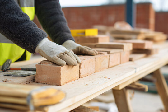 mason laying final brick courses while carpenters prepare roof structure materials