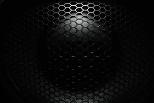 Close-up macro shot of a dark metallic speaker grill. Hexagonal honeycomb pattern with a textured surface. Industrial abstract background suitable for technology, audio, or automotive themes.