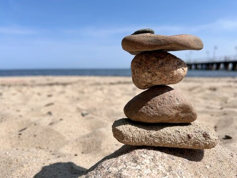 Balanced stack of smooth stones on sandy beach with blurred ocean and wooden pier in the background