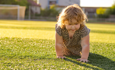 A young child with curly hair smiles while crawling on a green grassy surface The sun creates a warm glow illuminating the playful scene during late afternoon