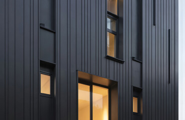 Obraz premium Minimalist urban duplex features flat black metal siding with linear shapes, narrow vertical windows. Modern architecture design creates sleek, contemporary exterior. Building exterior urban