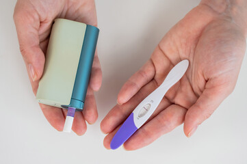 Woman holding pregnancy test and e-cigarette. 