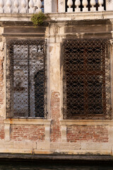 Window covered with an ornate and decorative metal security grill facing a canal in Venice