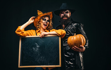 Halloween couple with pumpkin and Halloween makeup. Man and woman in witch hat celebrating...