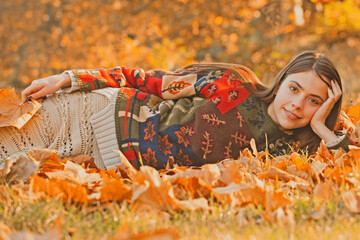 Autumn woman posing in golden sunlight. Stylish girl with fall leaves. Romantic portrait with autumn foliage. Model in autumn nature. Woman with falling leaves. Girl outdoor shoot in autumn park.