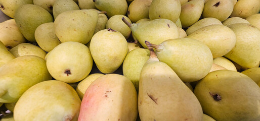Ripe yellow-green pears with smooth skin and natural spots are stacked closely together, showcasing...