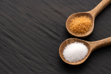 Brown sugar and refined white sugar in wooden spoons