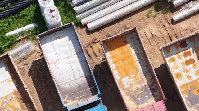 Close aerial shot of multiple dump trucks in various colors parked in rows on a dirt surface at a construction or industrial site.