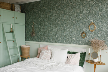 The interior of a classic bedroom. A bed with pillows and a wooden bedside table with dried flowers...