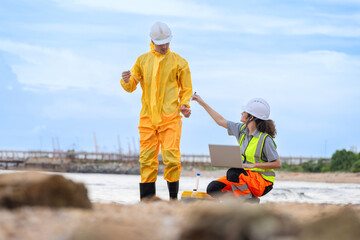 Environmental Scientists Collecting Water Samples for Analysis, Researchers in Protective Gear Studying Water Quality at Site, Ecologists Working on Beach, Monitoring Environmental Contamination