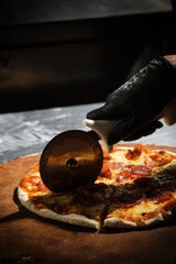 Chef slicing freshly baked pepperoni pizza with pizza cutter