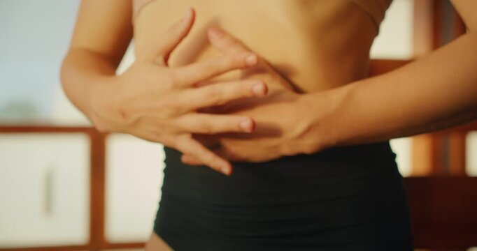Closeup of a woman midriff as she holds her belly during breathing exercises warmup movements