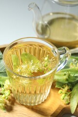 Tasty linden tea in cup, leaves and flowers on light table, closeup