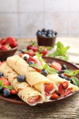 Tasty crepes with berries, cream and mint on wooden table, closeup