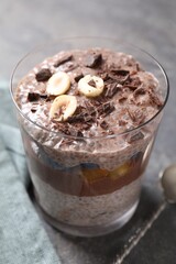 Delicious chocolate pudding with chia seeds, nuts and berries in glass on grey table, closeup