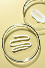 Different cosmetic products in Petri dishes on pale yellow background, flat lay