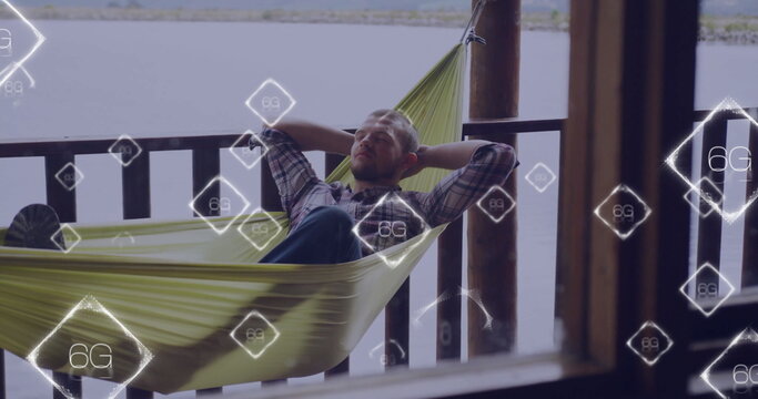 Reclining male in shirt viewing 6G icons on green hammock between wooden posts at lakeside porch - Powered by Adobe