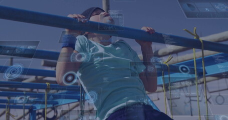 Pulling up boy wearing headband and wristbands on metal bars at obstacle course, yellow rope nets