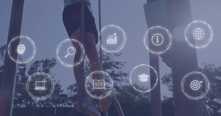Climbing two boys gripping braided ropes on outdoor obstacle course, with digital learning icons