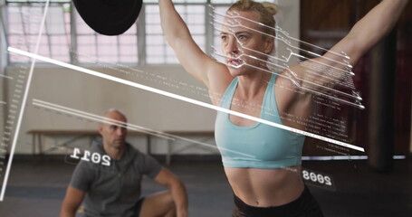 Lifting female athlete raising barbell overhead at gym, with wooden benches and padded flooring