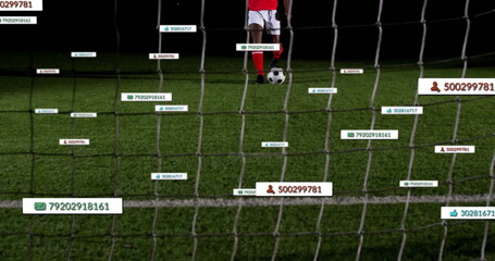 Soccer player in red jersey preparing to kick ball on nighttime pitch, with goal net, tags